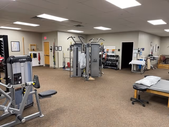 Interior rehab gym at Magnolia Regional Outpatient Rehab Center with exercise machines and a treatment table.