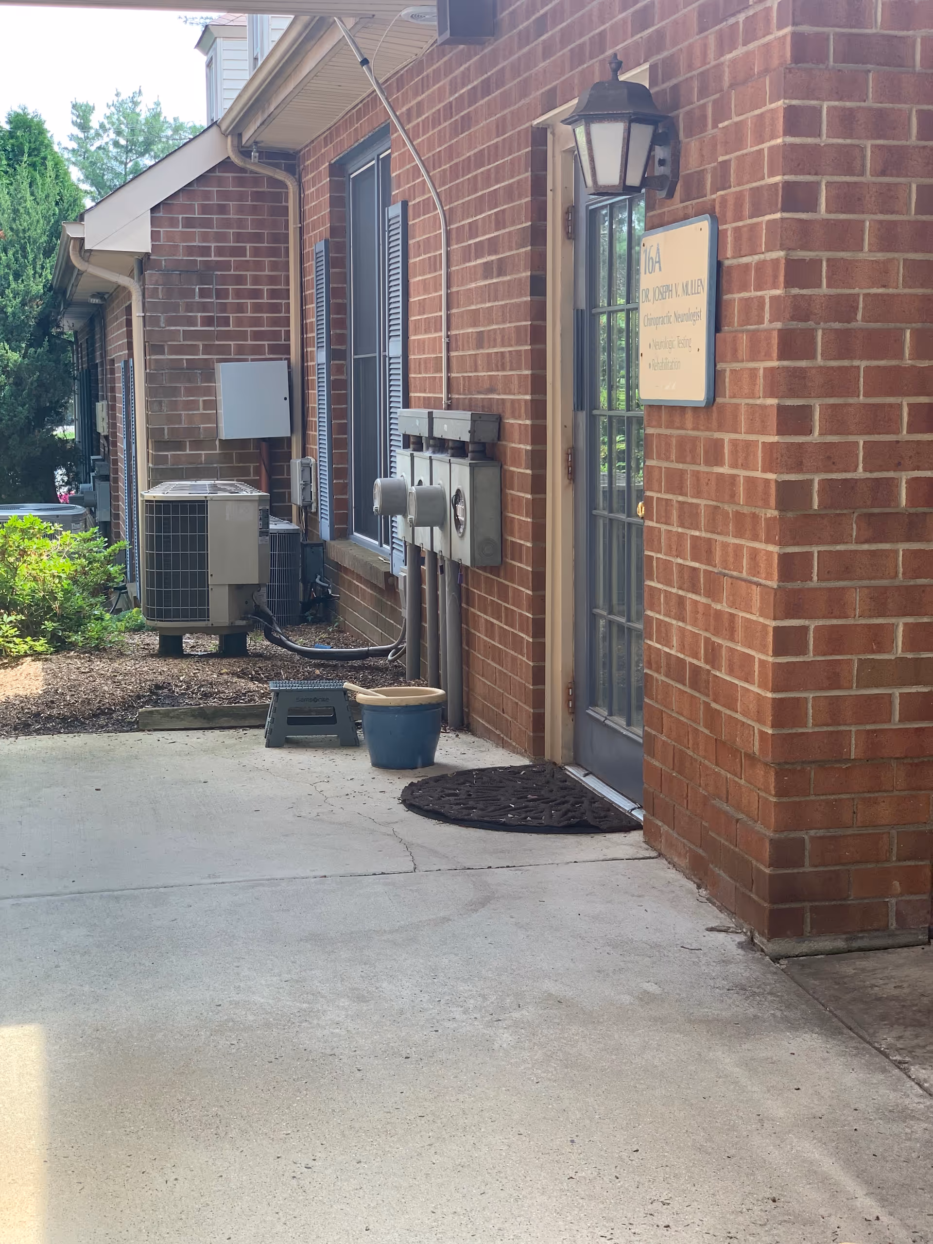 Brick exterior of a senior living facility with a door, sign, and outdoor utility equipment.