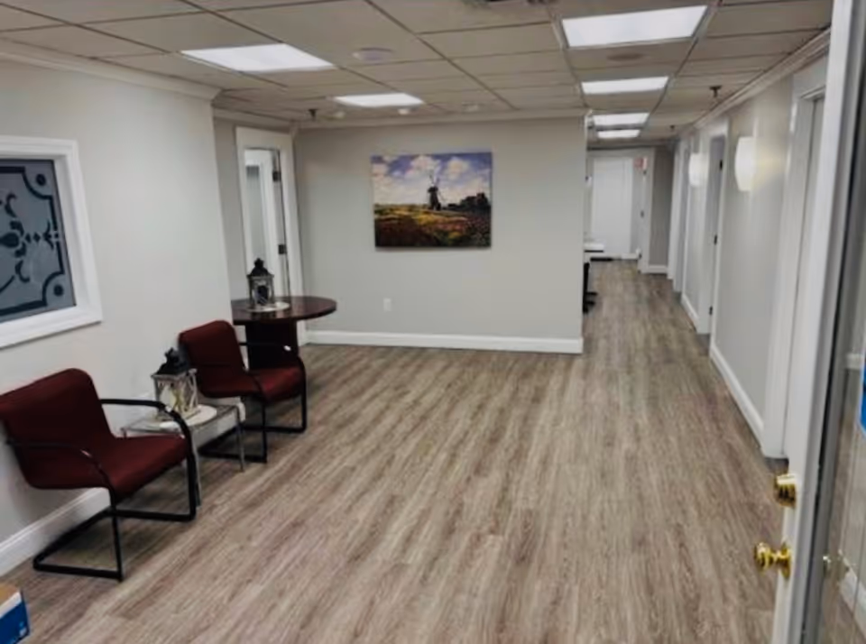 Long hallway inside a senior facility with seating area, wall art, and wood-like flooring.