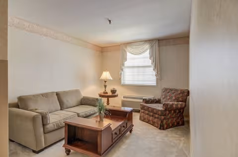 Cozy beige living room with sofa, armchair, coffee table, and lamp.