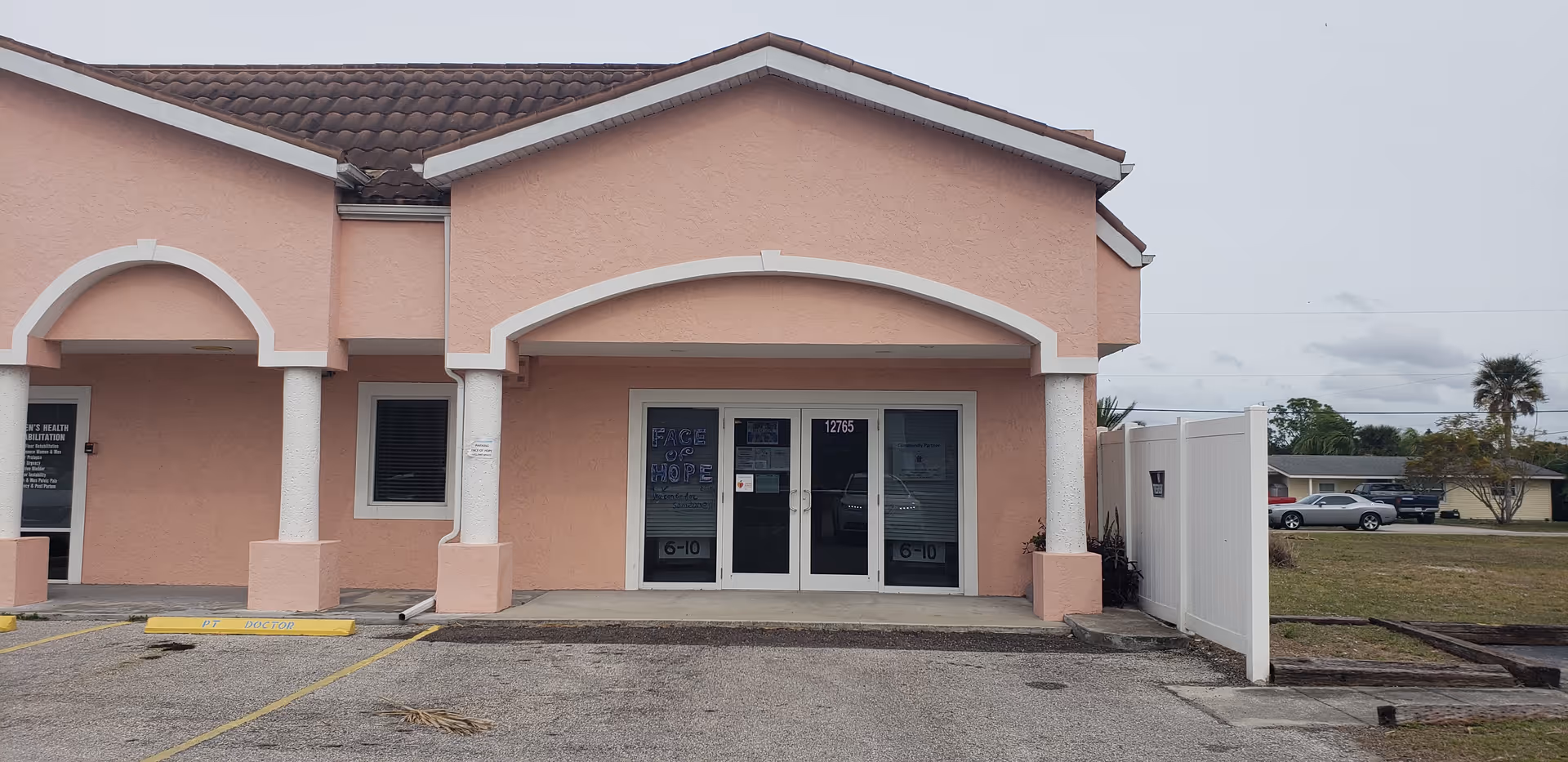 Front view of a pink senior living facility with arches, porch columns, and glass doors.