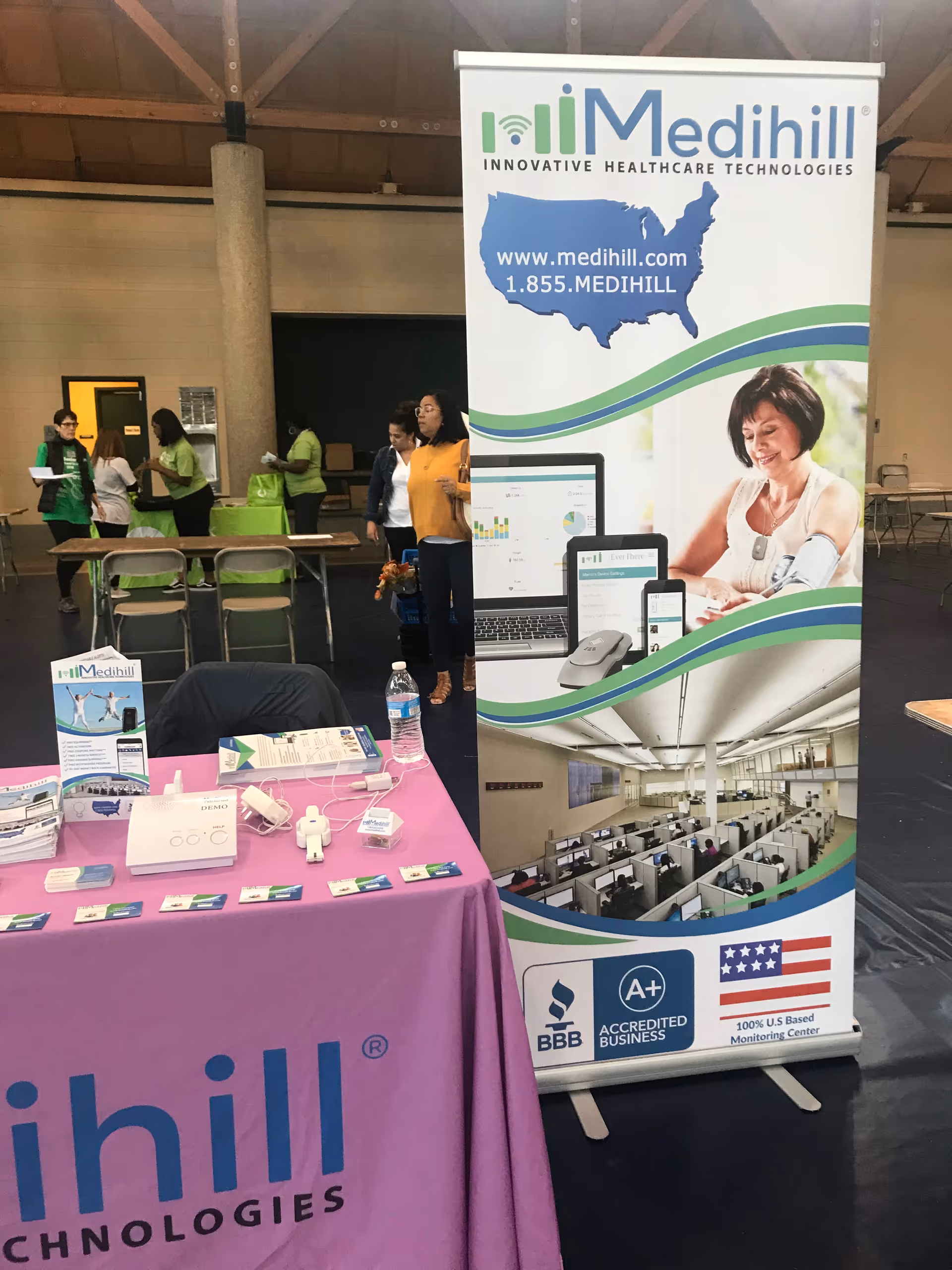 Tall Medihill banner beside a purple table with medical devices at an indoor event.