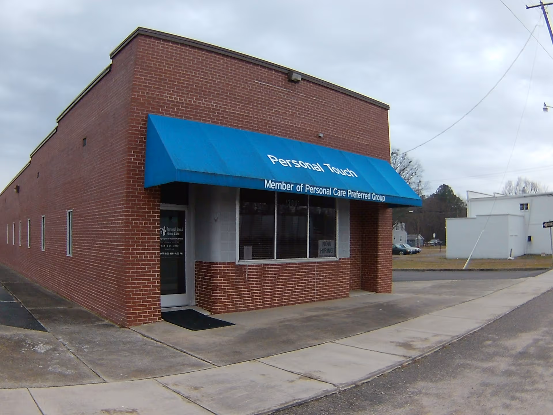 Brick building storefront with blue awning displaying Personal Touch Home Care Services.