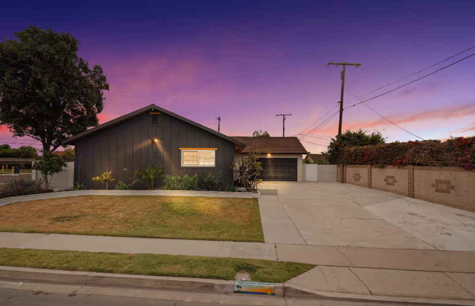 Exterior of a single-story, dark senior living building with a driveway at sunset.