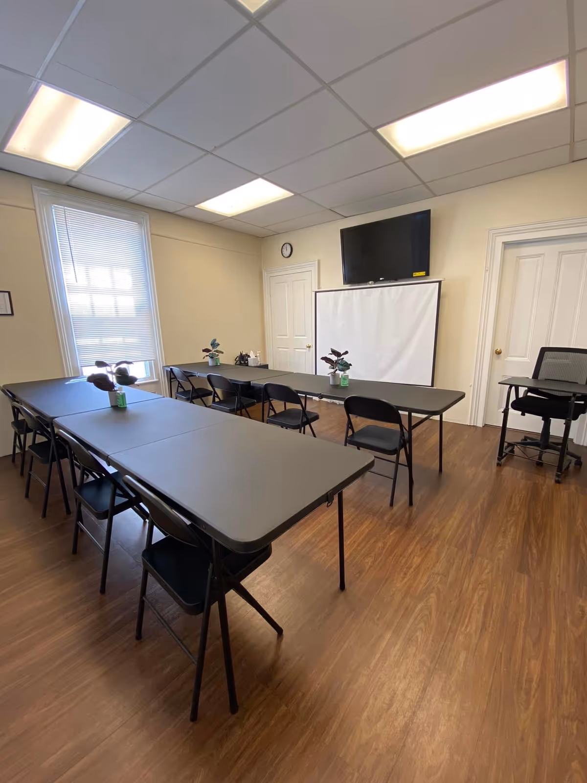 Interior meeting room with long gray tables, black chairs, projector screen, and TV.