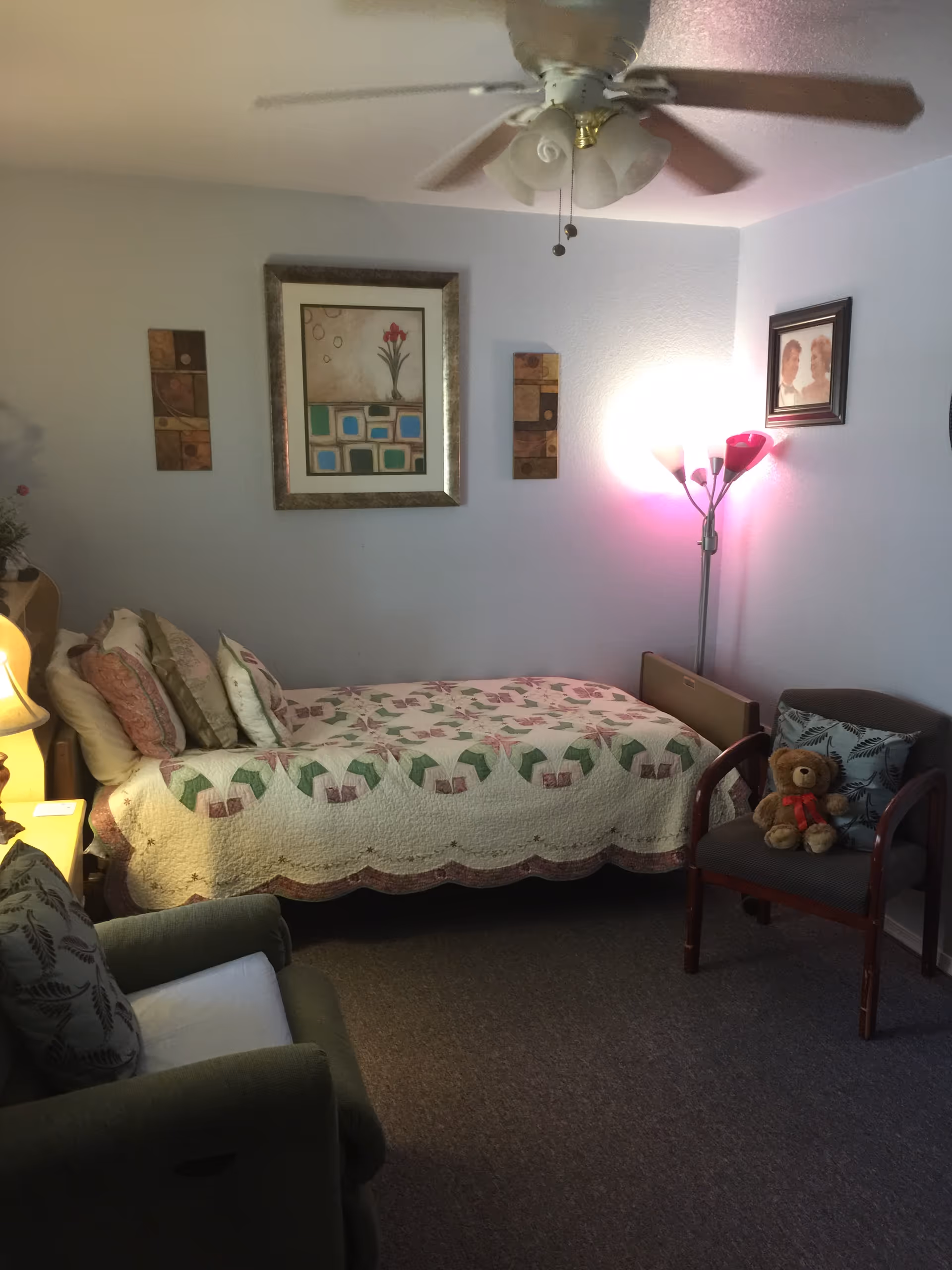 Cozy bedroom with quilted bed, seating, and a ceiling fan under soft lighting.