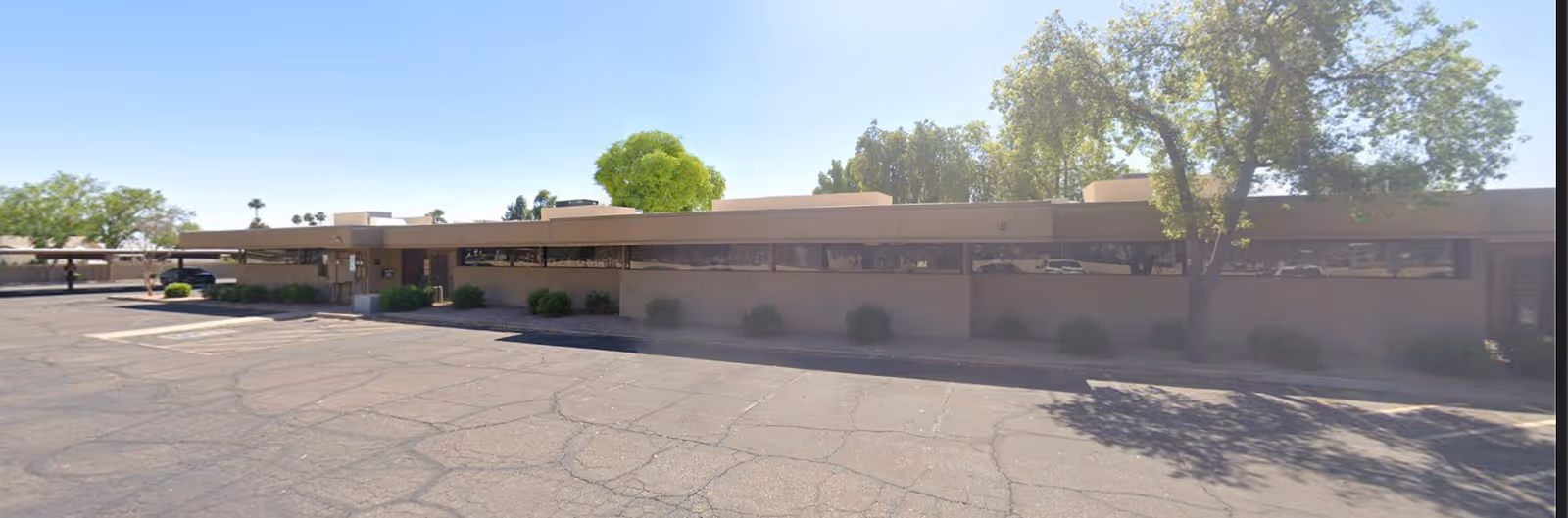Single-story beige senior care building with a large parking lot and trees.
