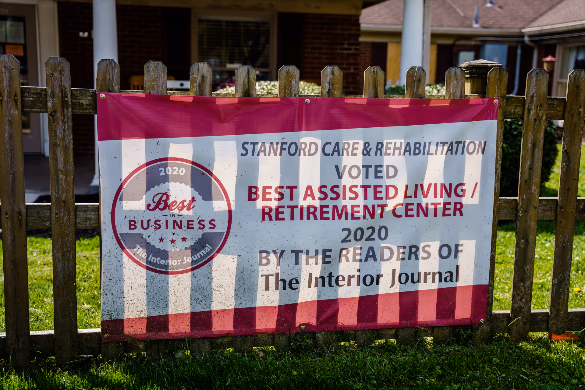 Banner advertising Stanford Care and Rehabilitation on a wooden fence in front of the building.