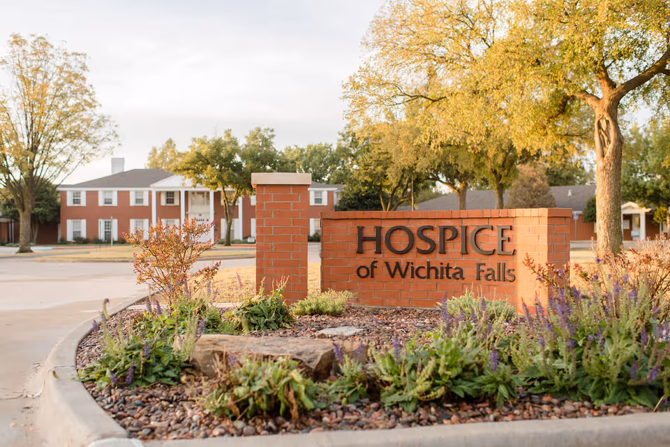 Brick sign for Hospice of Wichita Falls with landscaped foreground and building in background.