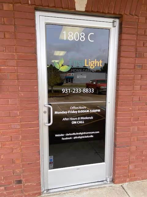 Glass door with FirstLight Home Care logo, address 1808 C, and contact details on brick exterior.