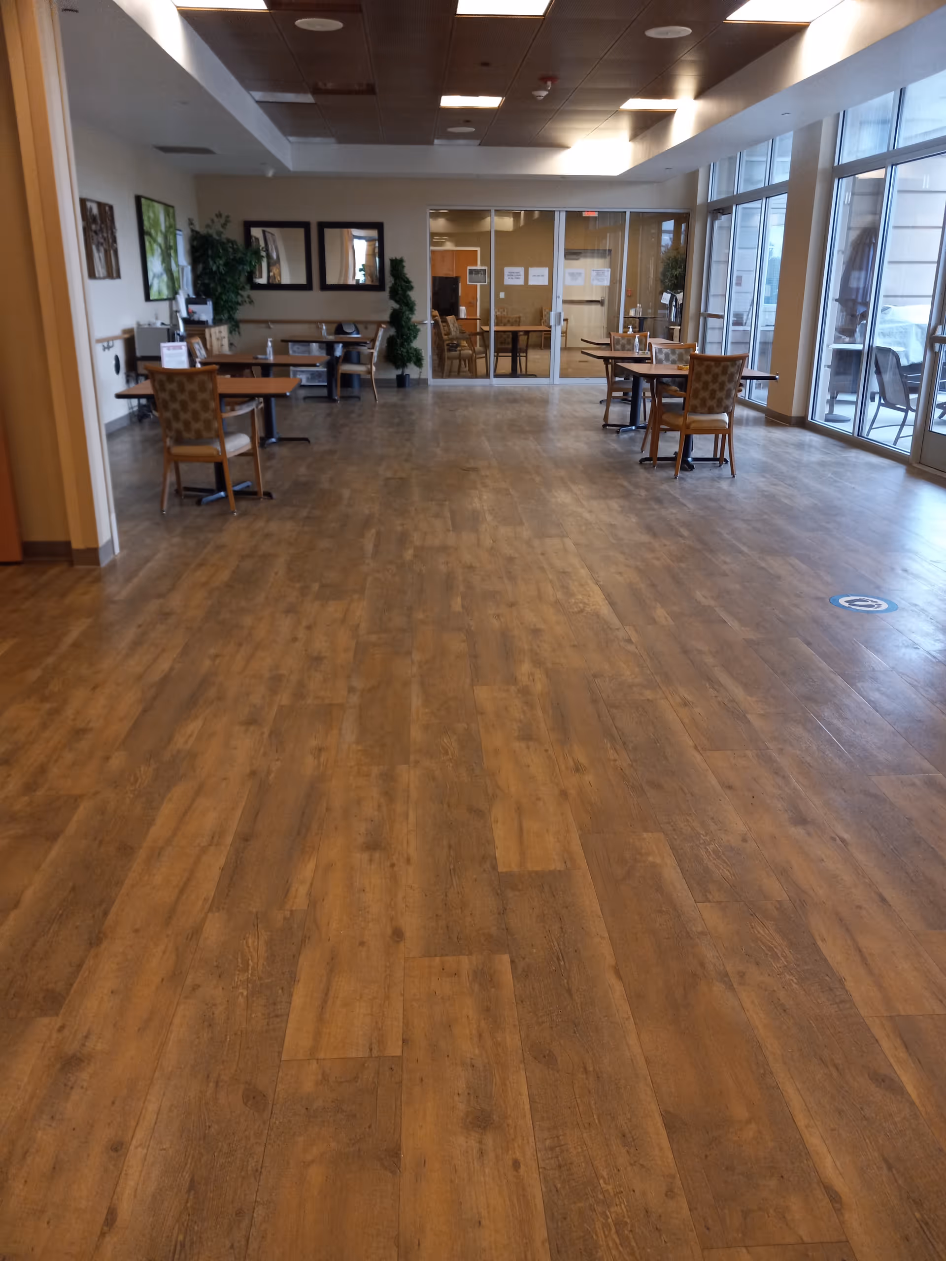 Spacious senior living common area with tables, chairs, and glass doors at the back.