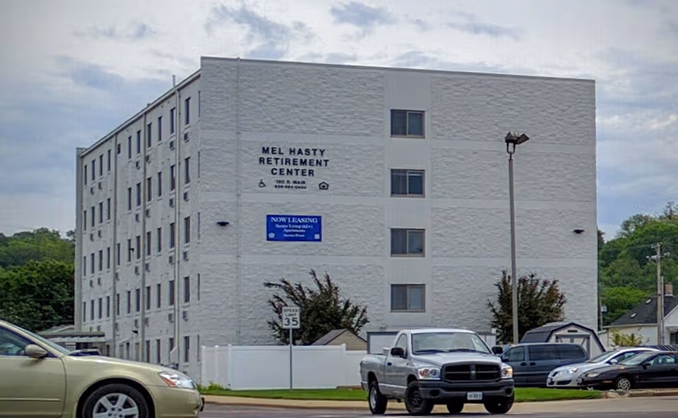 Exterior of Mel Hasty Retirement Center, a white multi-story facility with parked cars.