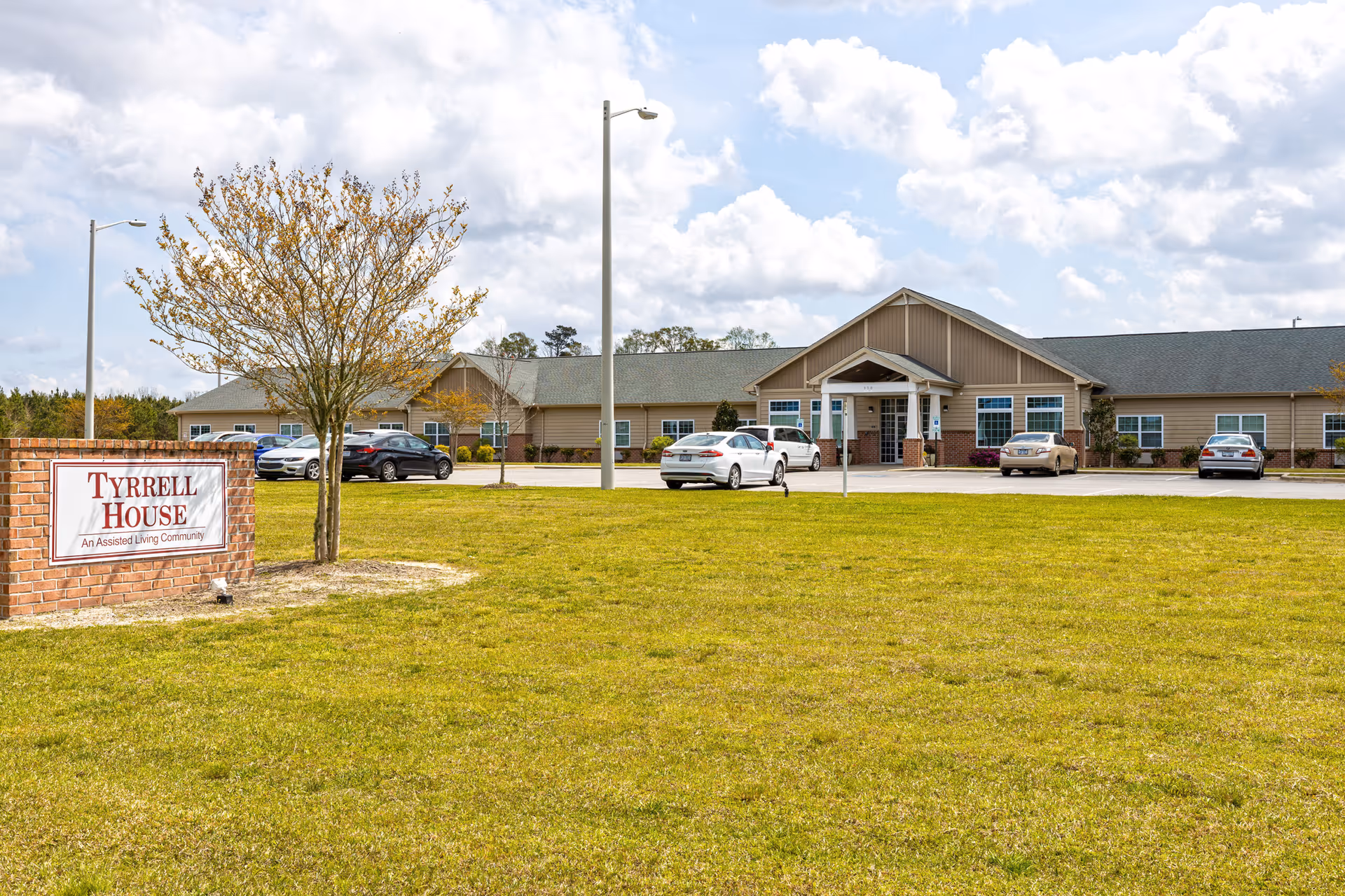 Exterior view of Tyrrell House assisted living facility with sign, lawn, and parked cars.