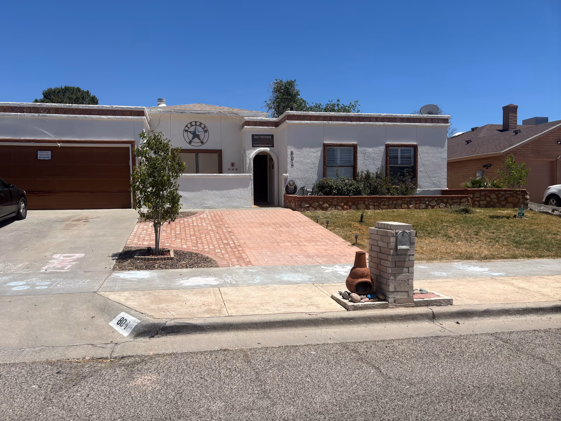 Single-story white building labeled Adult Foster Homes with brick-paved front walkway and yard