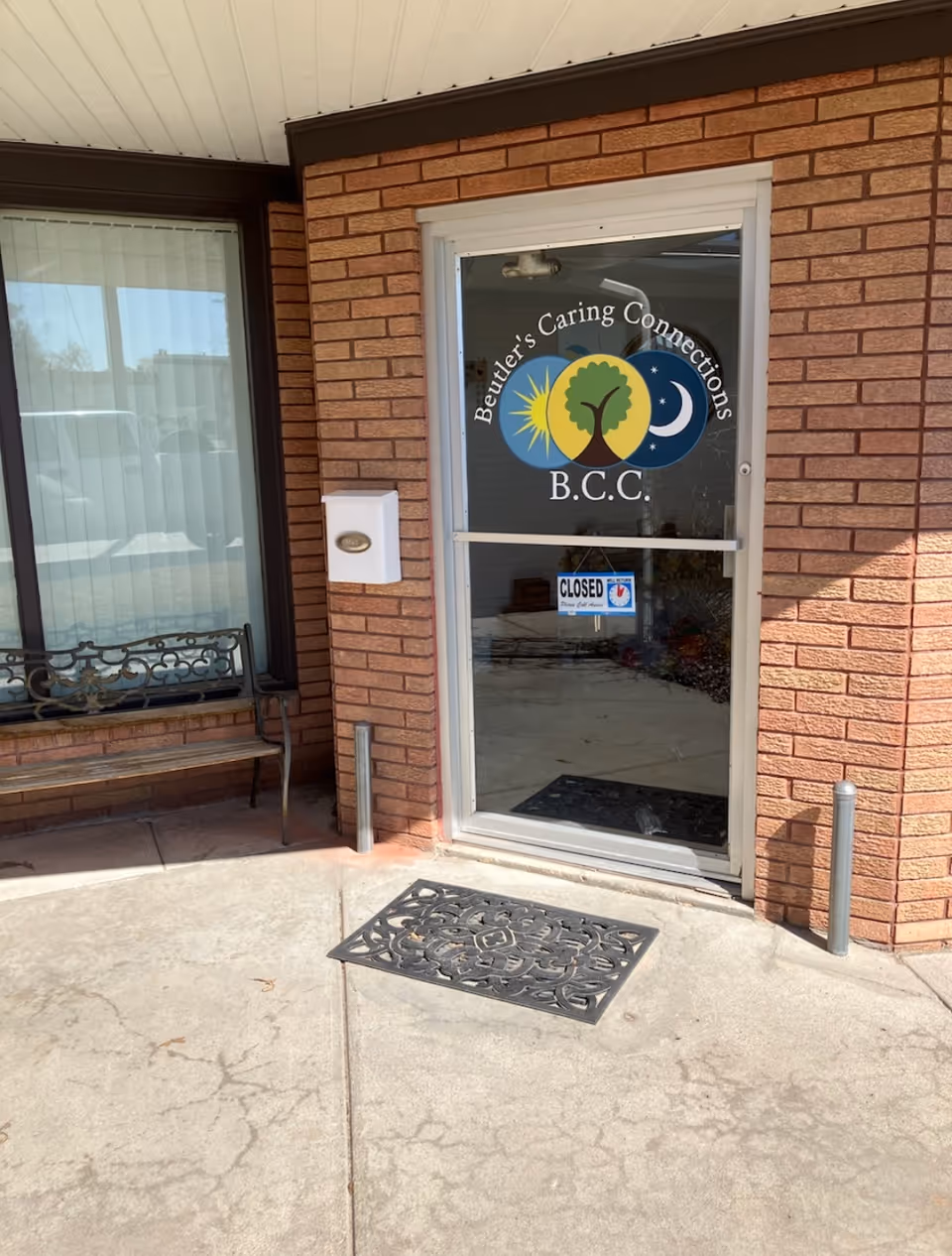 Brick exterior entrance featuring Beutler's Caring Connections door and a bench.