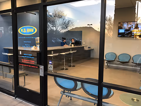 Inside a reception area with M.D. NOW signage and two staff at a counter behind glass.