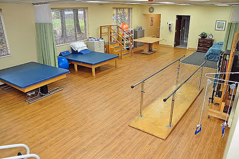 A rehabilitation/physical therapy room with parallel bars, treatment tables, therapy stairs and exercise equipment.