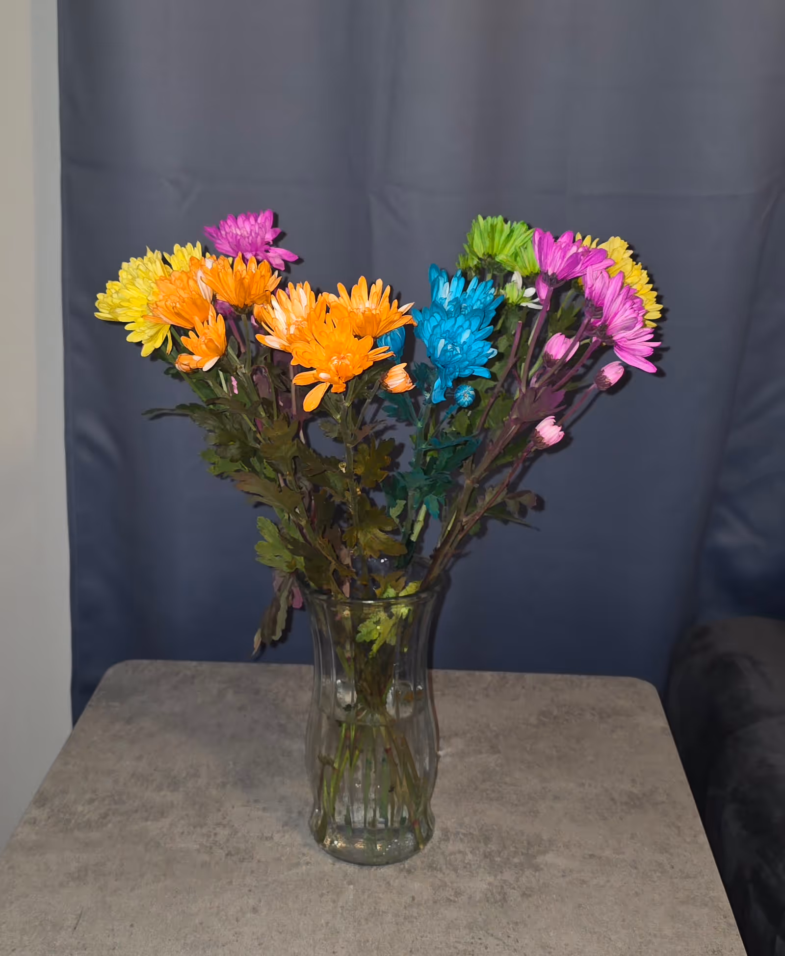 Colorful bouquet of artificial flowers in a glass vase on a gray table.