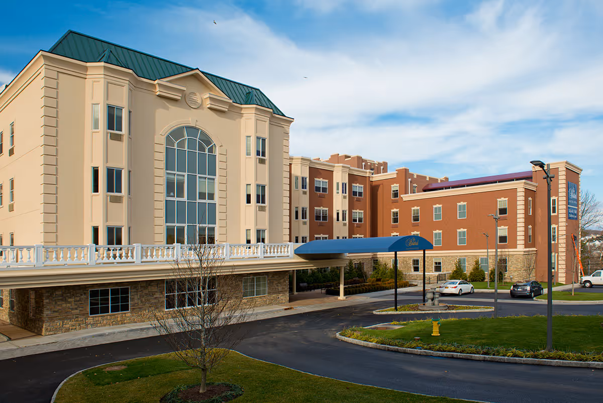 Front exterior of a multi-story assisted living building with a covered entrance canopy and driveway.