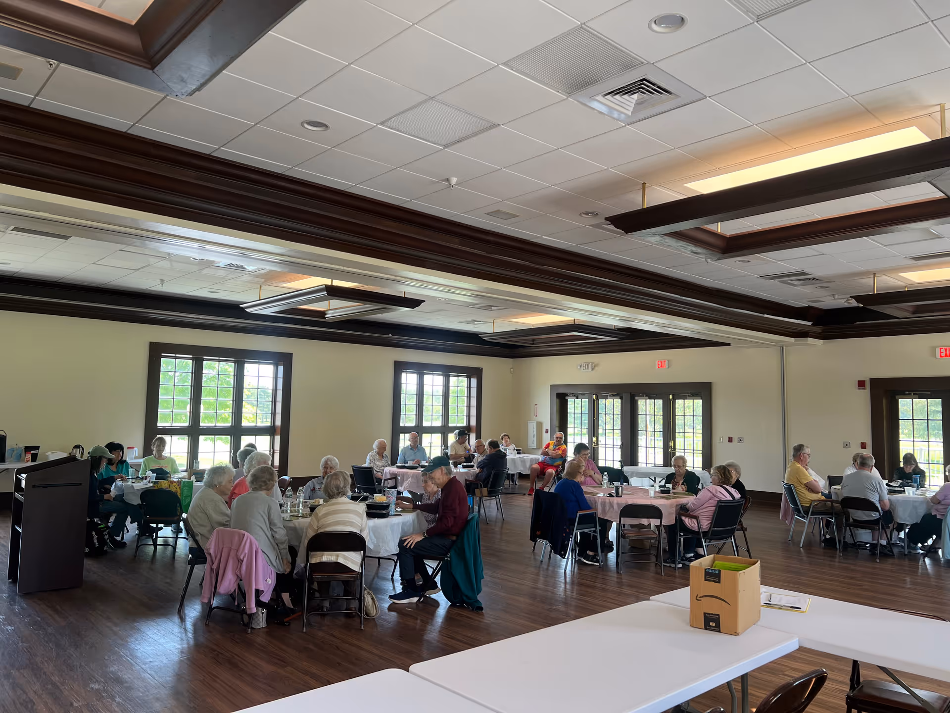 A spacious senior living dining room with residents seated at tables for a meal.