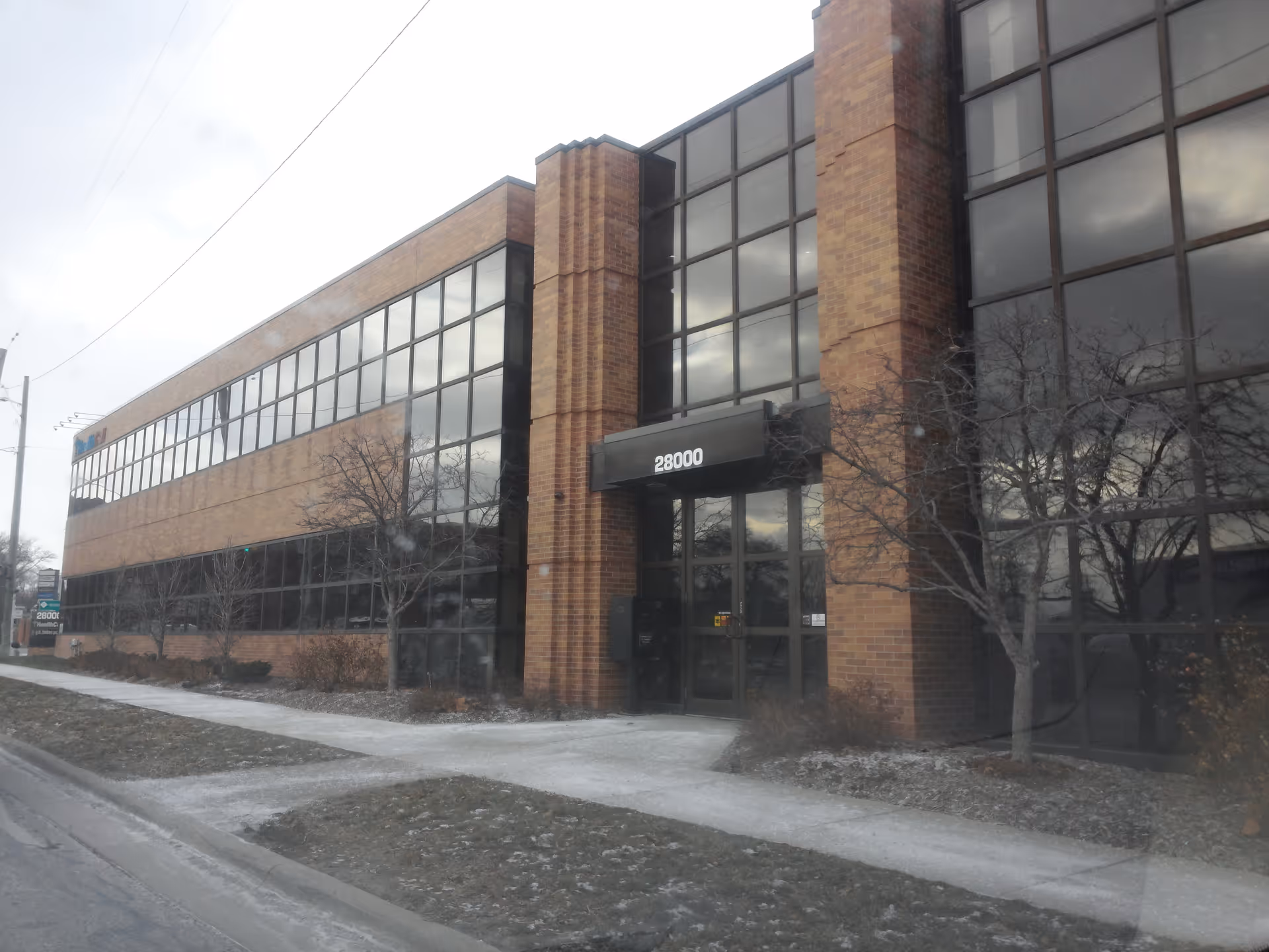 Front view of a brick office building with large glass windows and a black entrance canopy.