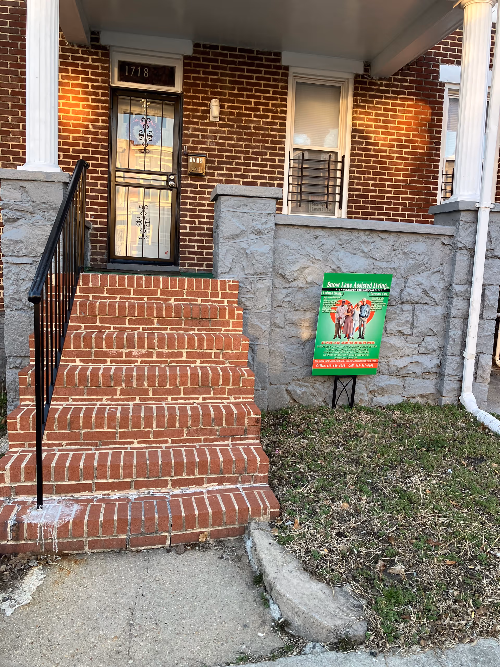 Brick front entrance of Snow Lane Assisted Living with steps, railing, and sign.