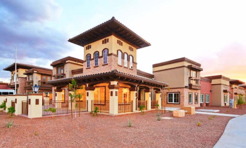 Exterior front view of Mediterranean-style senior living buildings with courtyards and desert landscaping.