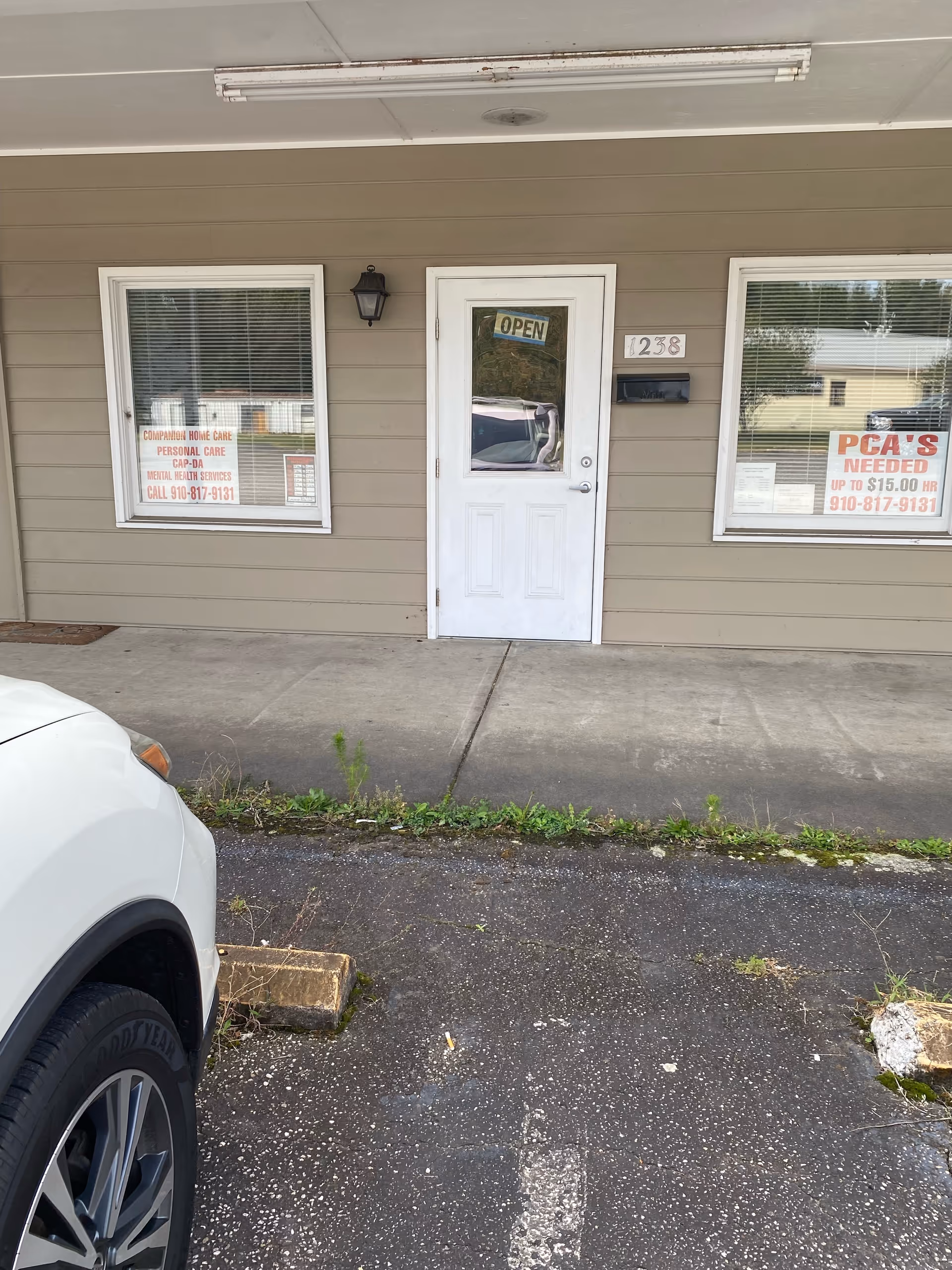 Plain beige building front with white door, windows, signs for Companion Home Care and open sign.