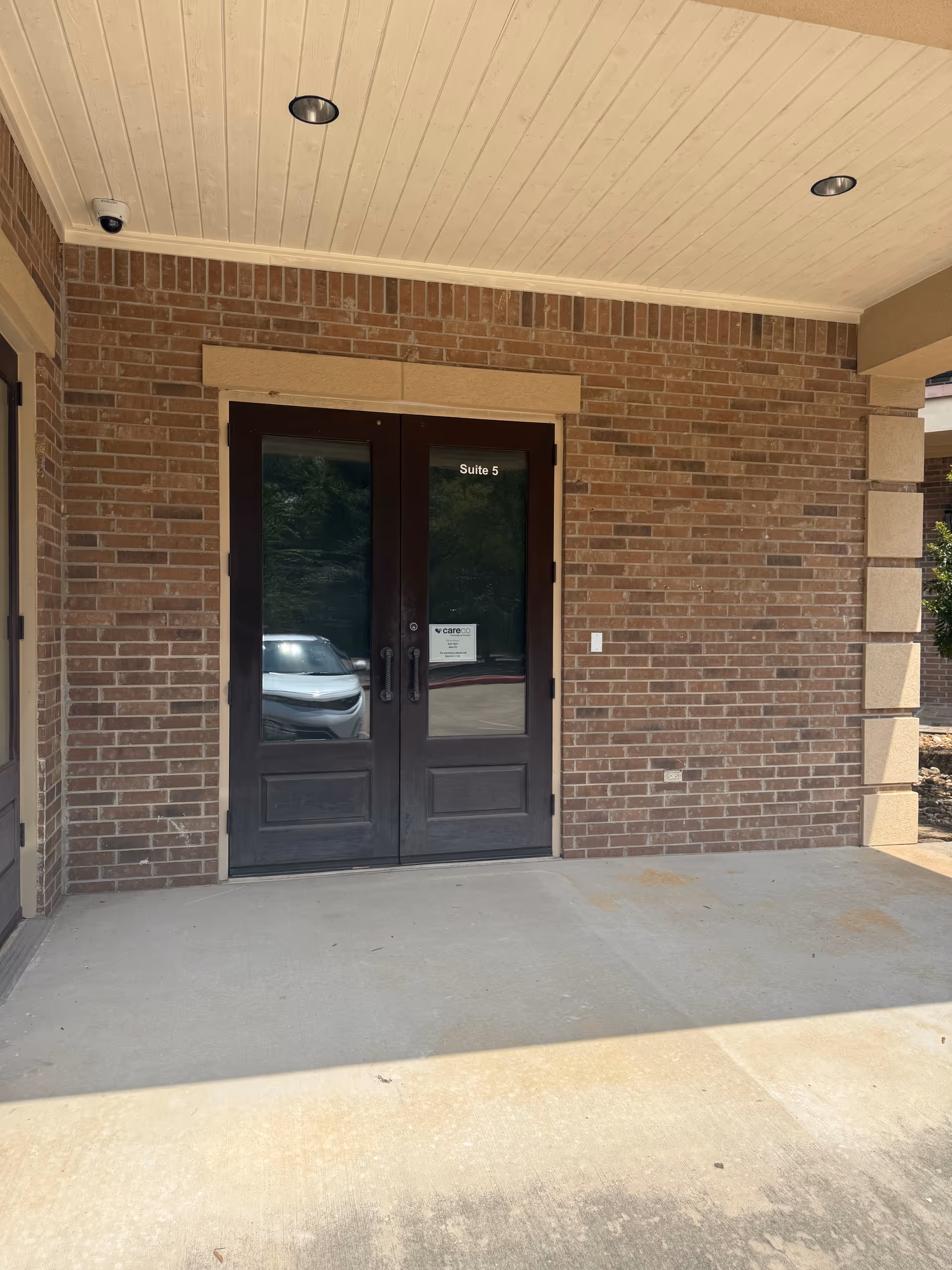Double dark doors labeled Suite 5 sit in a brick building entrance under a white canopy.