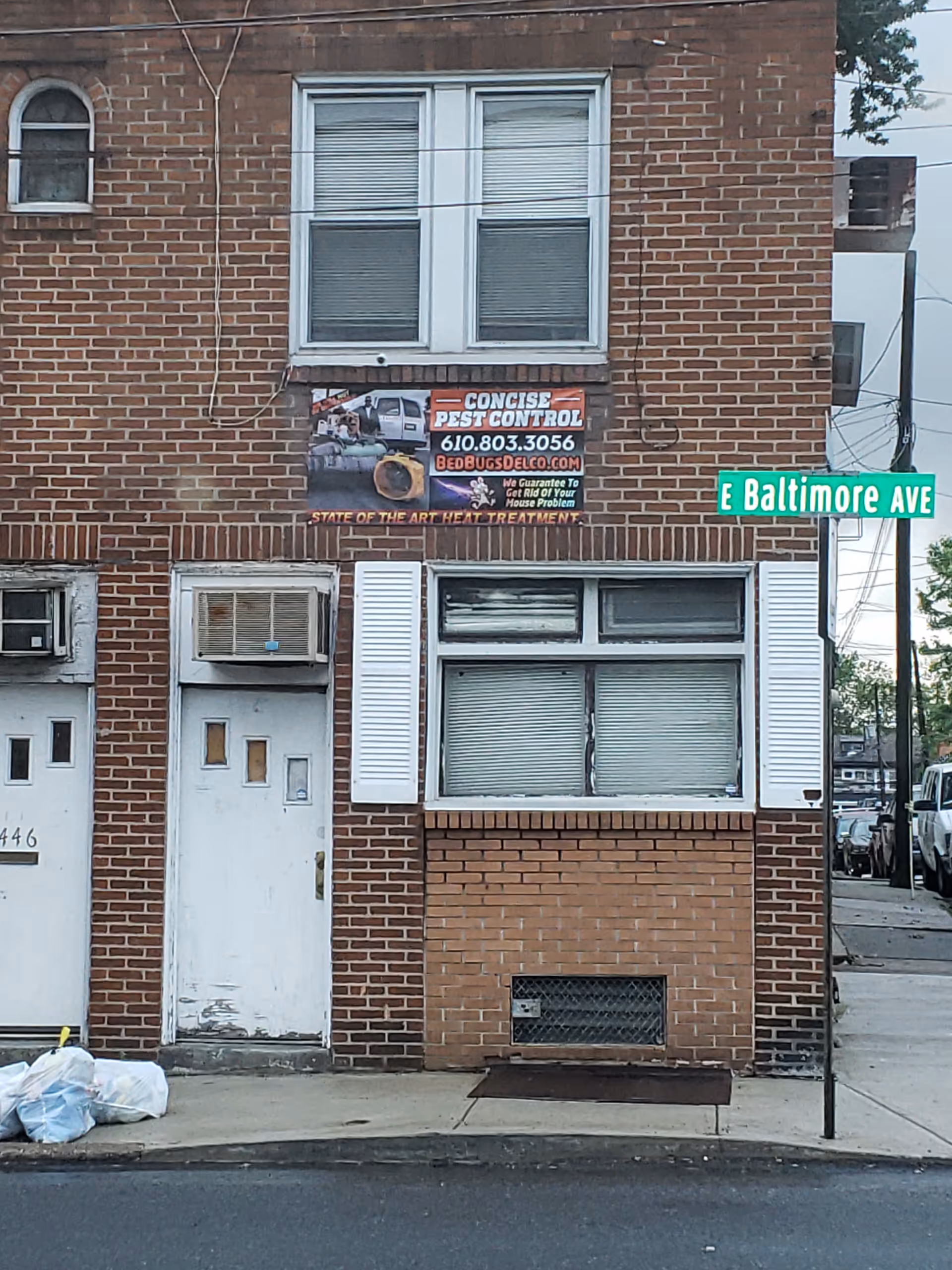 Two-story brick building with a pest control banner and a Baltimore Avenue street sign.