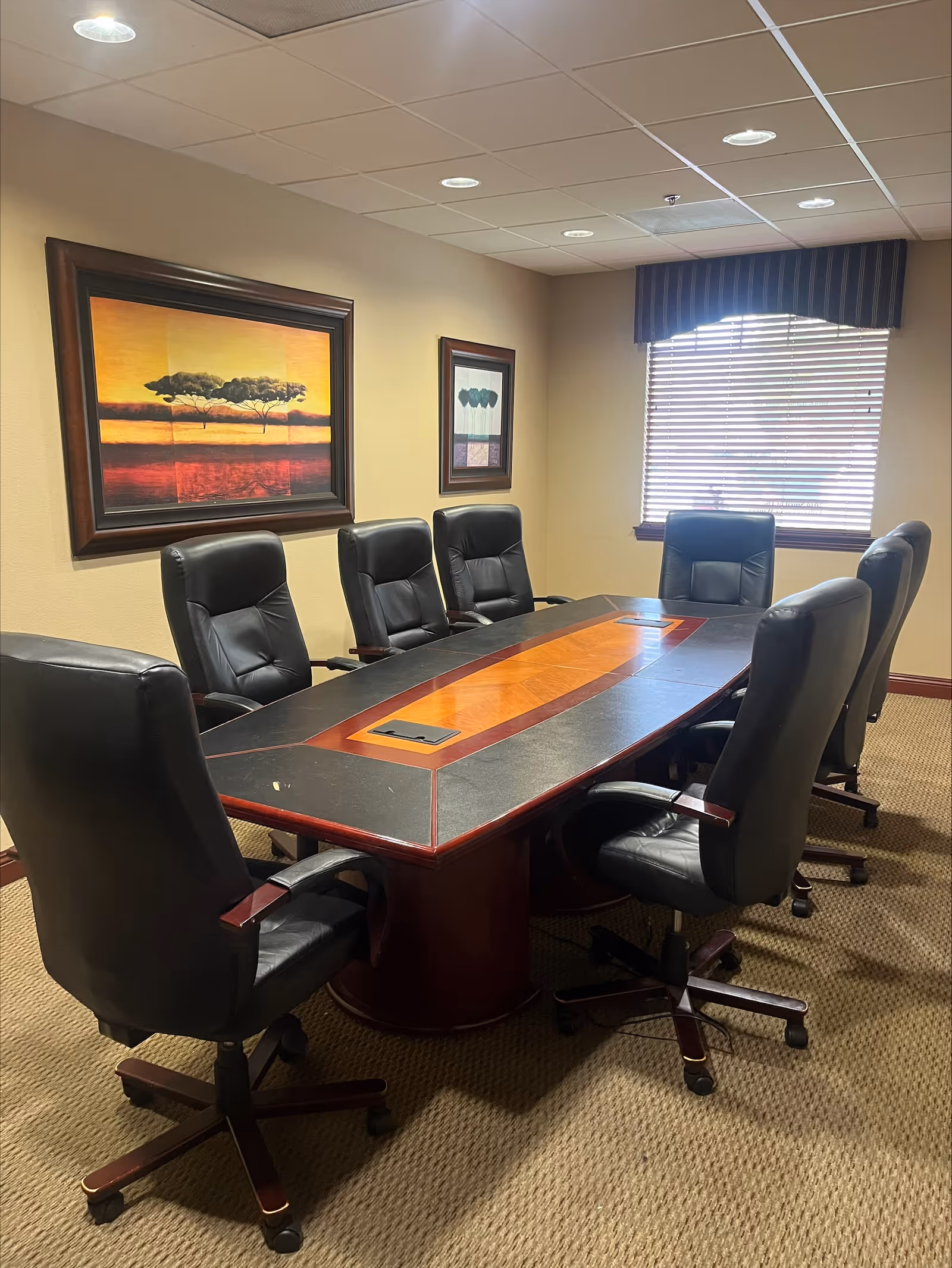 Conference room with long table, black leather chairs, wall art, and window blinds.