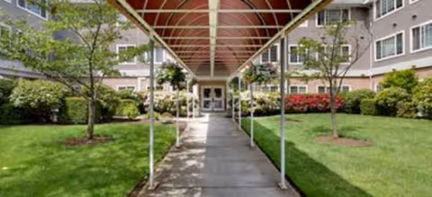 Covered walkway leads to the entrance of a senior living building with green lawns.