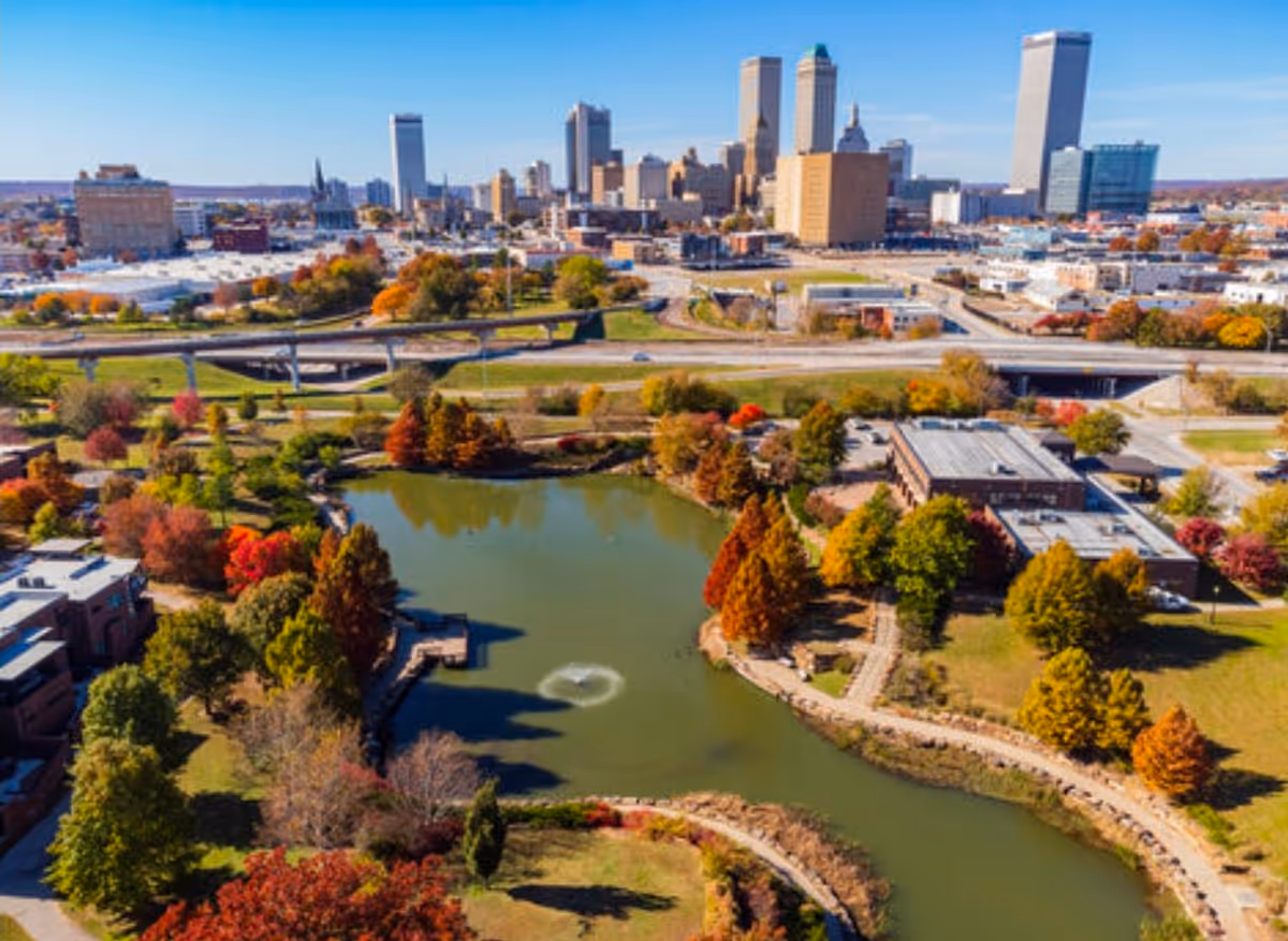 Aerial view of Tulsa skyline above a winding park lake with autumn-colored trees