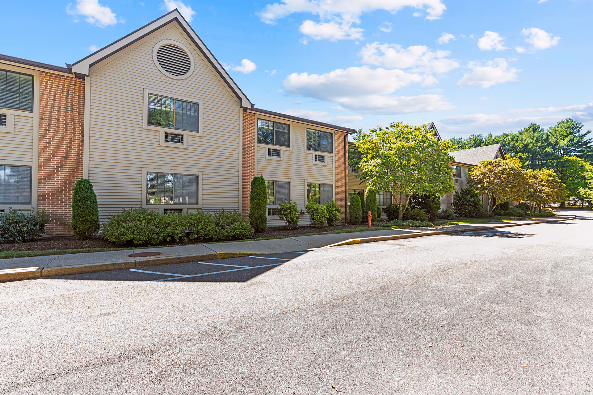 Two-story senior living facility with beige siding and brick accents along a landscaped front.