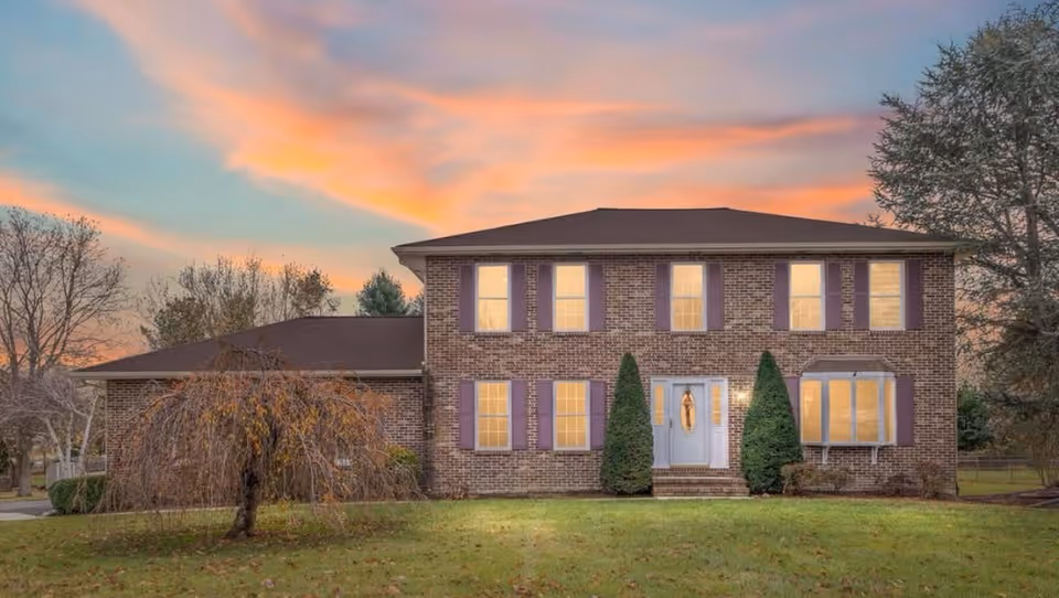 Front exterior view of a brick two-story building with purple shutters and trimmed shrubs.