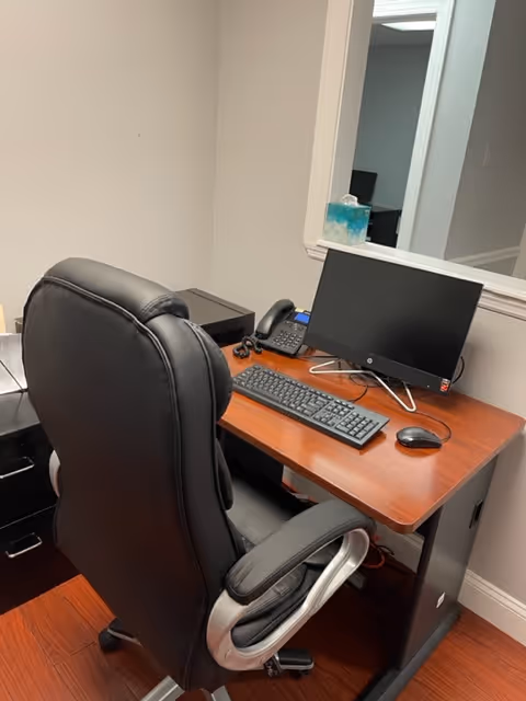 Office desk with computer, keyboard, mouse, and leather chair.