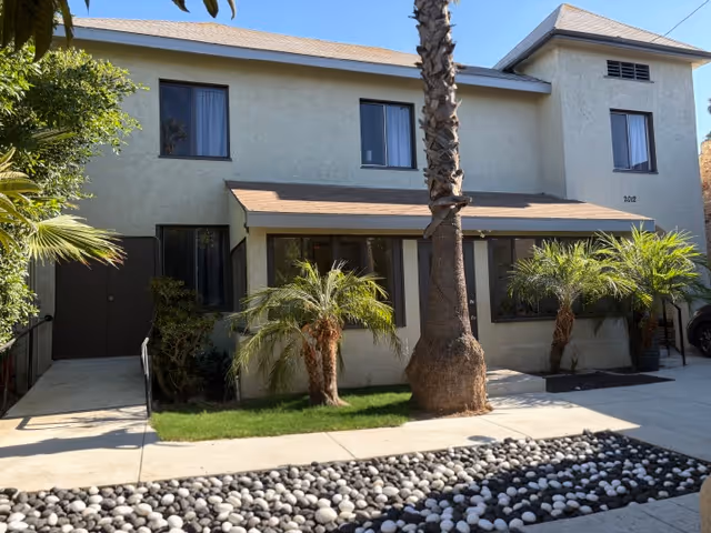 Two-story beige senior living facility exterior with palm trees and landscaped rock beds.