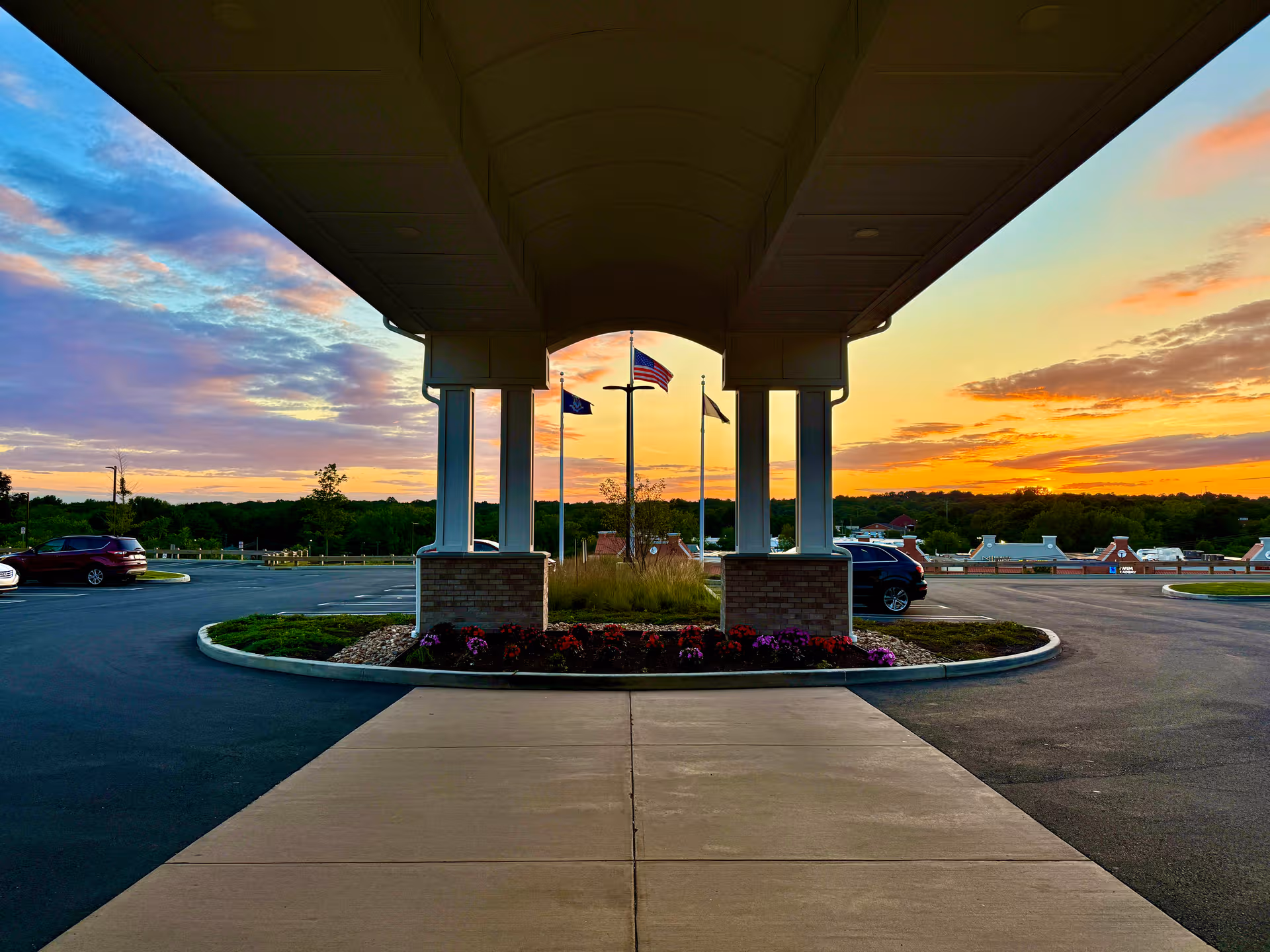 Covered driveway entrance with columns and flagpoles at sunset outside a senior living facility.
