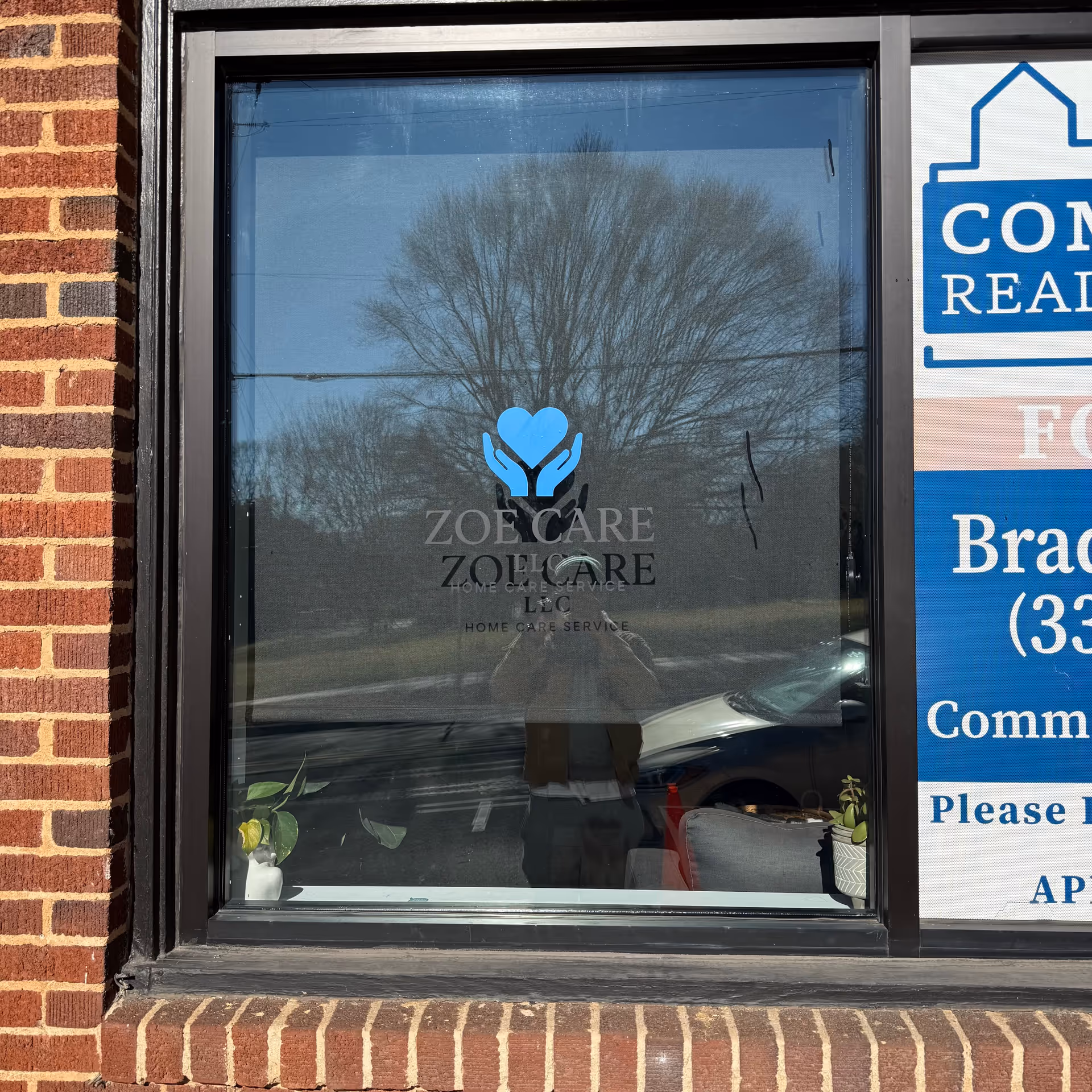 Front window of ZoeCare Home Care Services with logo, brick facade, and reflections.