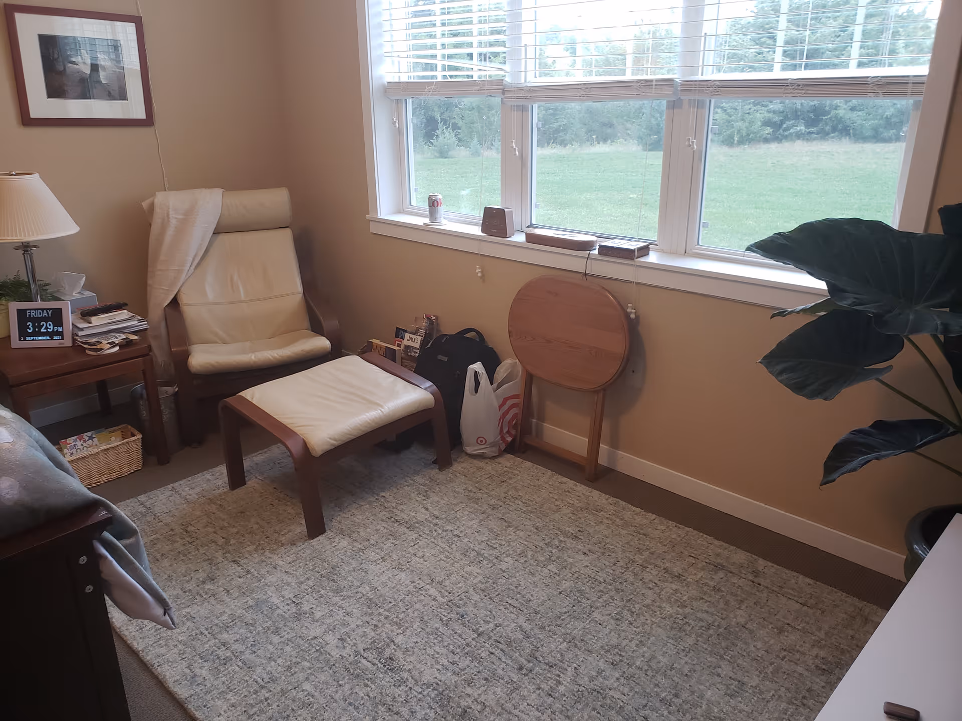 Cozy resident living area with beige chair, ottoman, side table, and large window view.