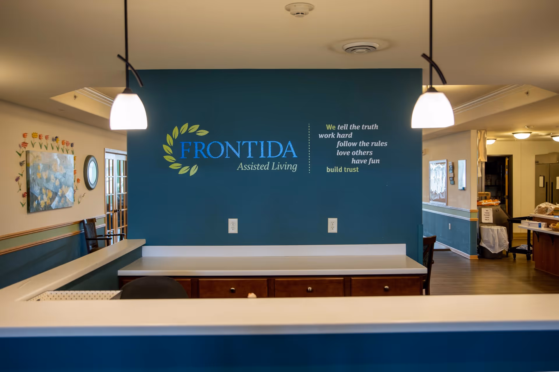 Reception area with teal front desk wall and Frontida logo in a senior living lobby.