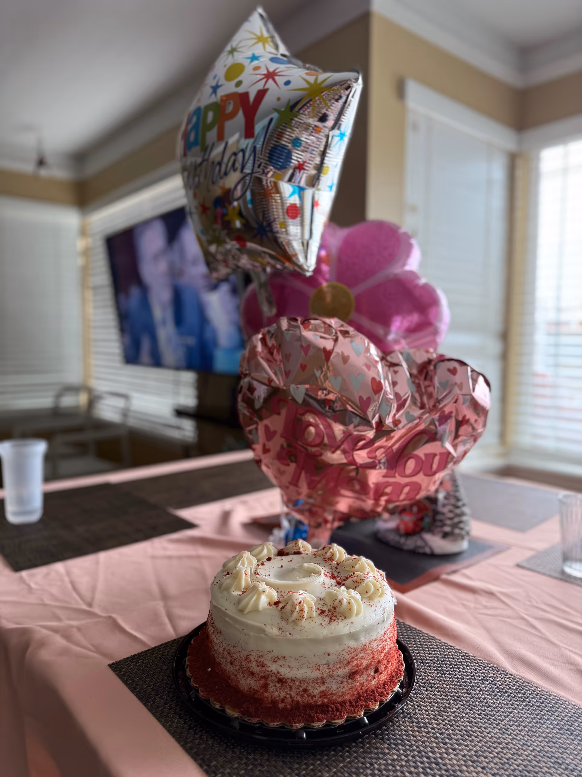 Birthday cake on a pink table with balloons in a cozy living room.