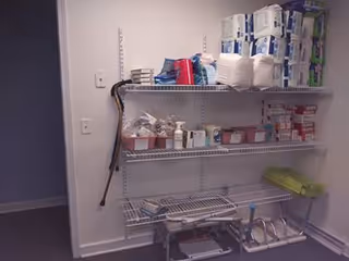 Small supply closet with metal shelves stocked with medical supplies and a cane nearby.