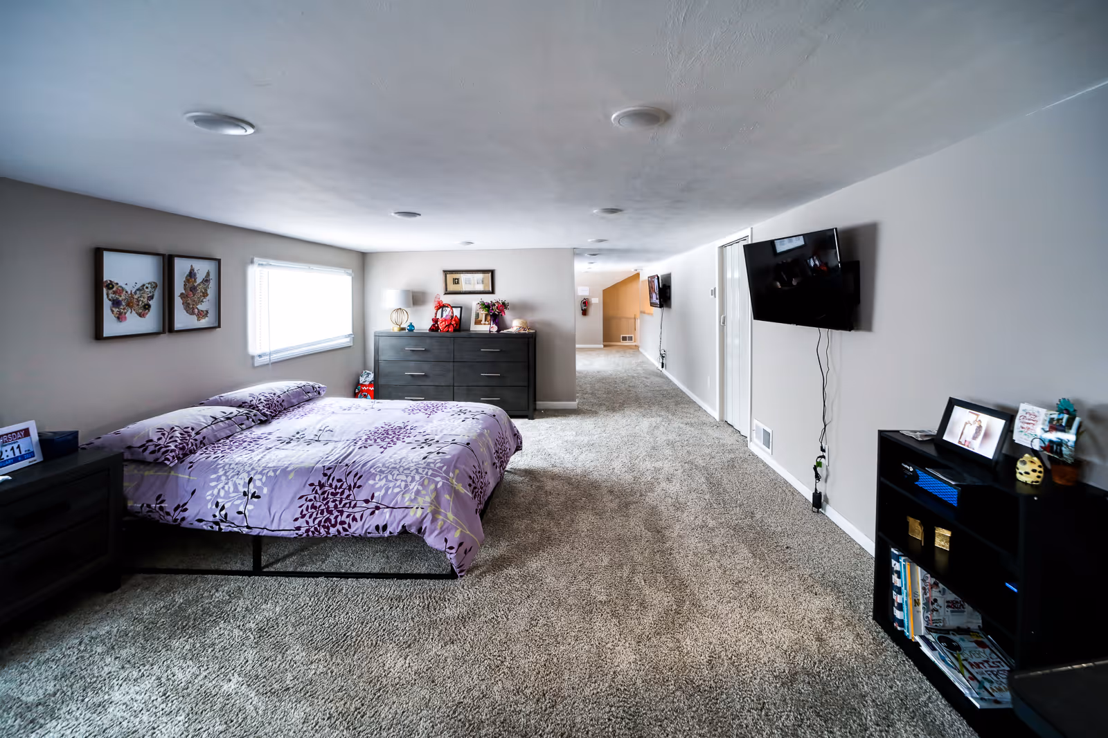 Cozy bedroom with purple patterned bedspread, dresser, and wall-mounted TV.