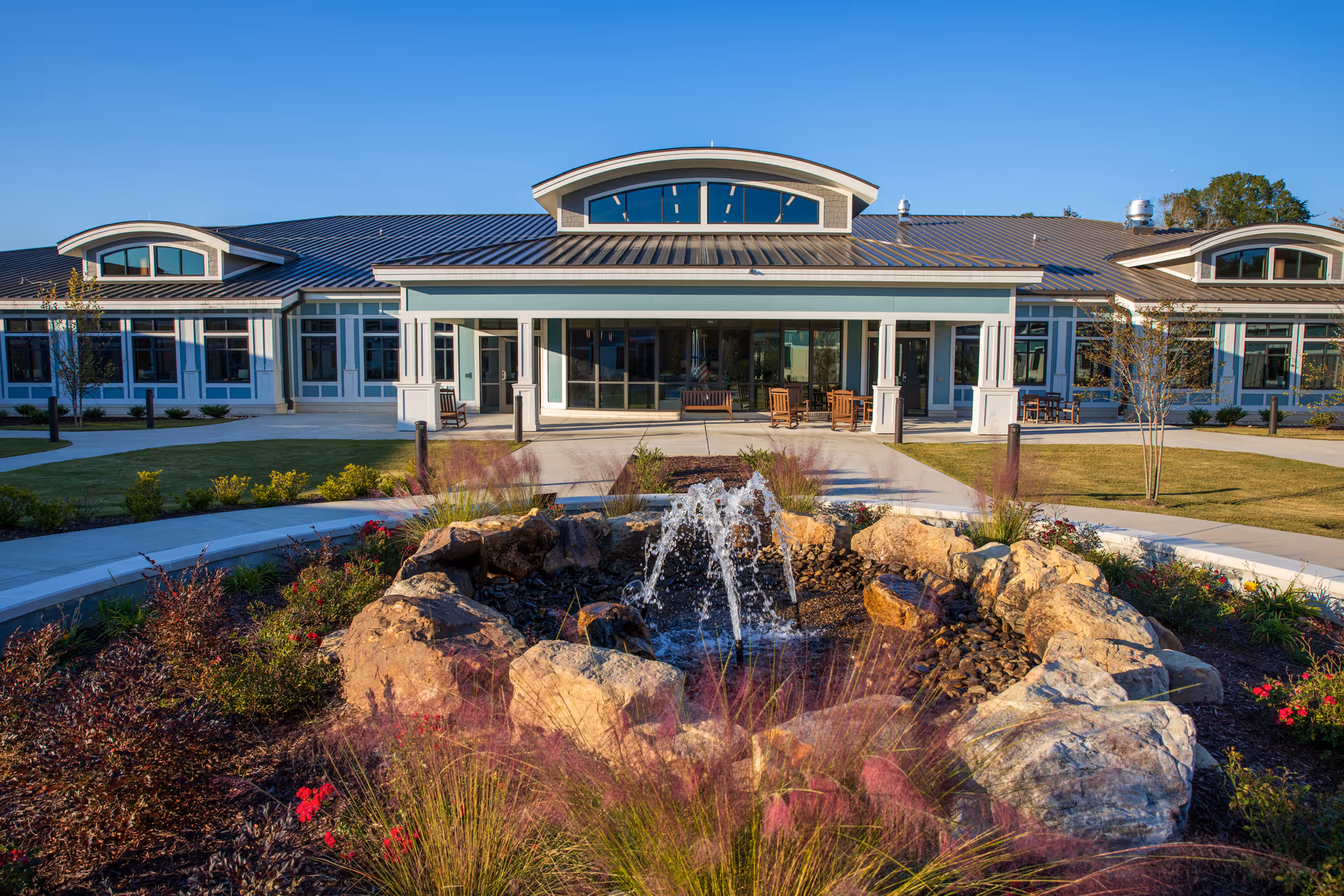Front view of a senior living facility with a fountain and outdoor seating area.