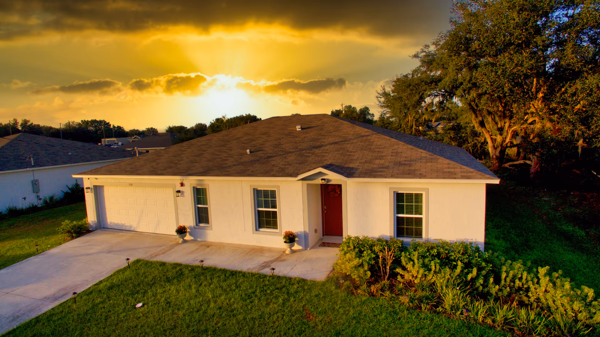 A single-story white house exterior with a red front door and attached garage at sunset.