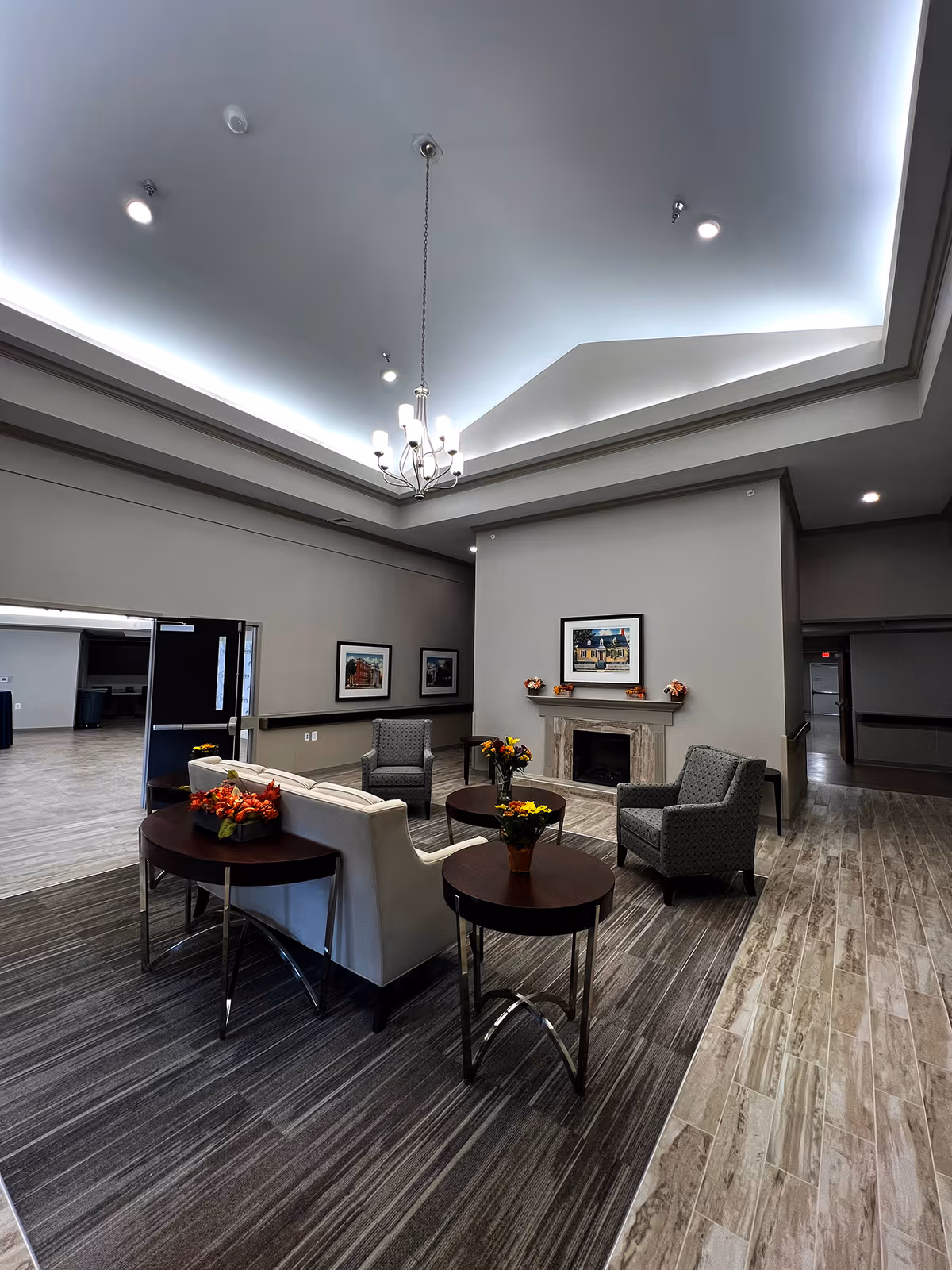 Elegant senior living lounge with sofas, armchairs, tables, fireplace, art, and chandelier lighting.