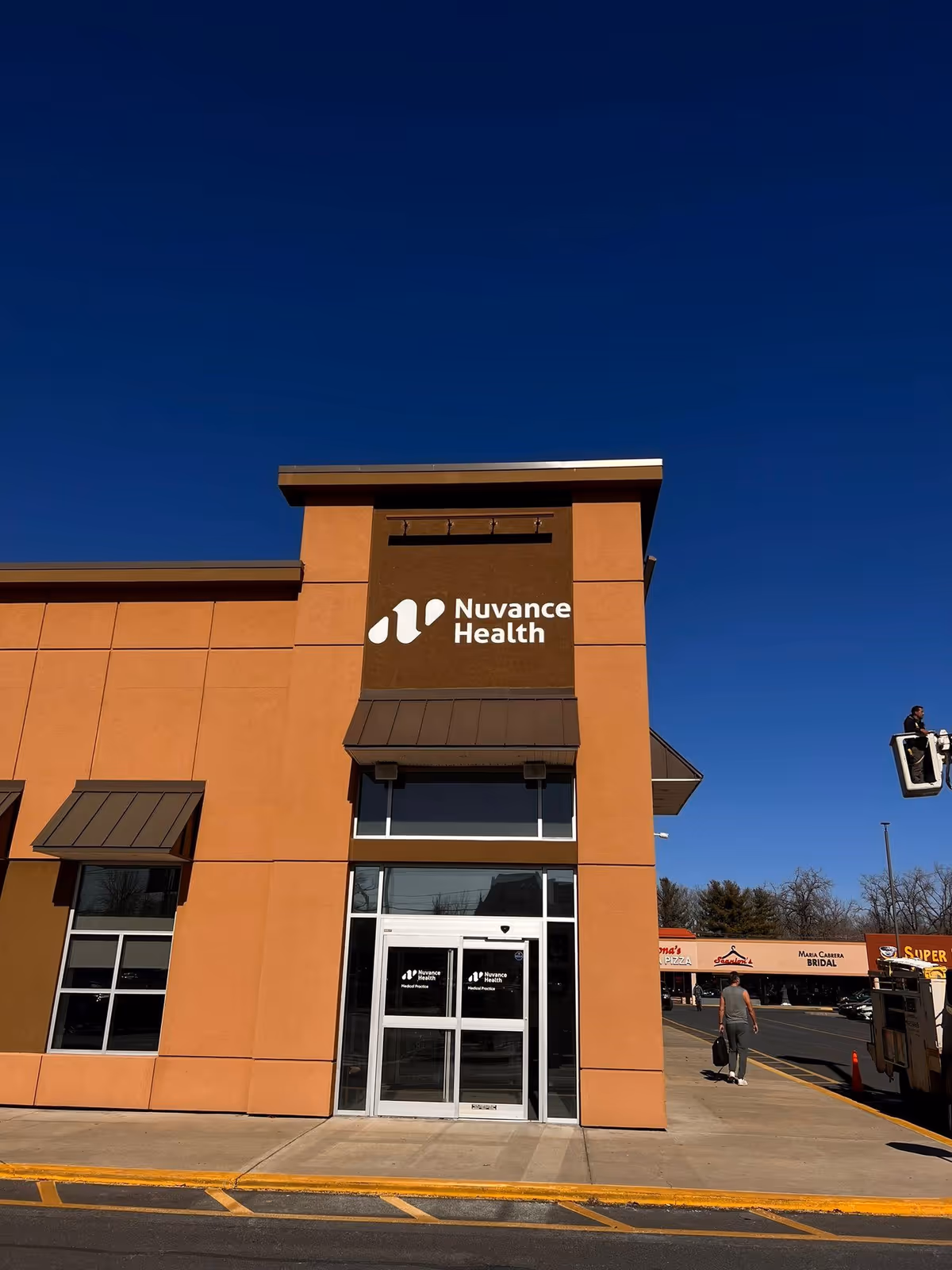 Orange brick building with Nuvance Health sign and glass entrance against blue sky.