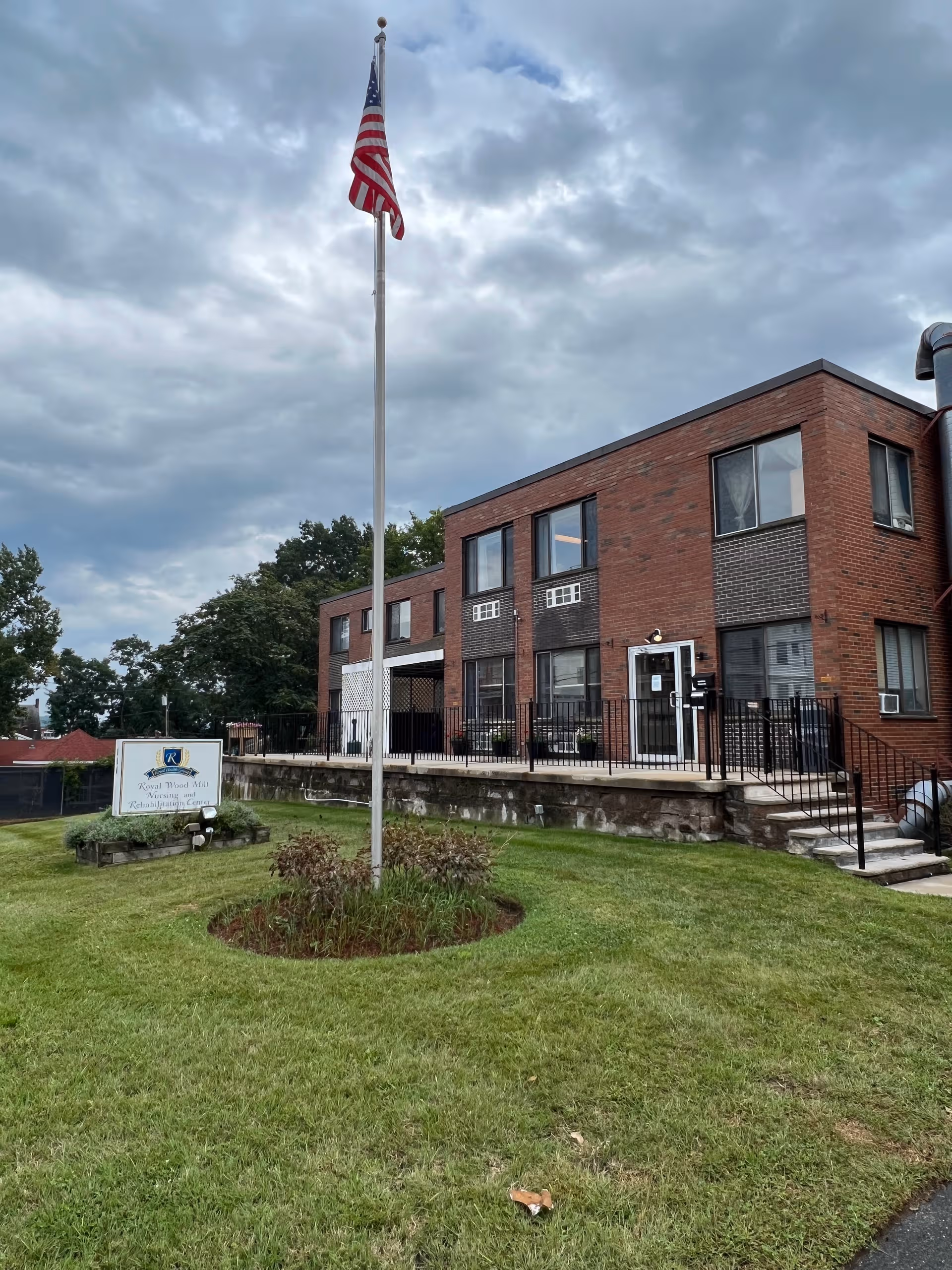 Brick nursing and rehabilitation center exterior with flagpole and manicured lawn.