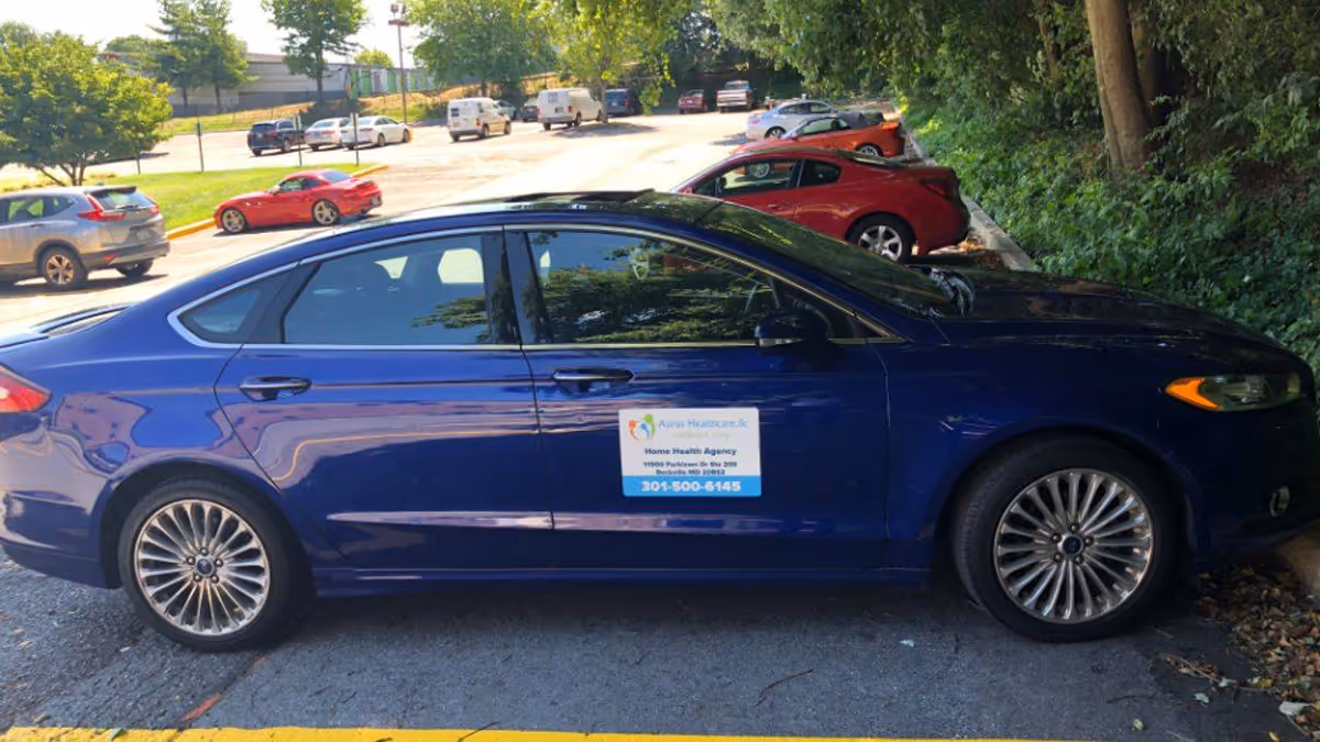 Blue sedan parked in a lot with an Aurus Healthcare sign on its door.